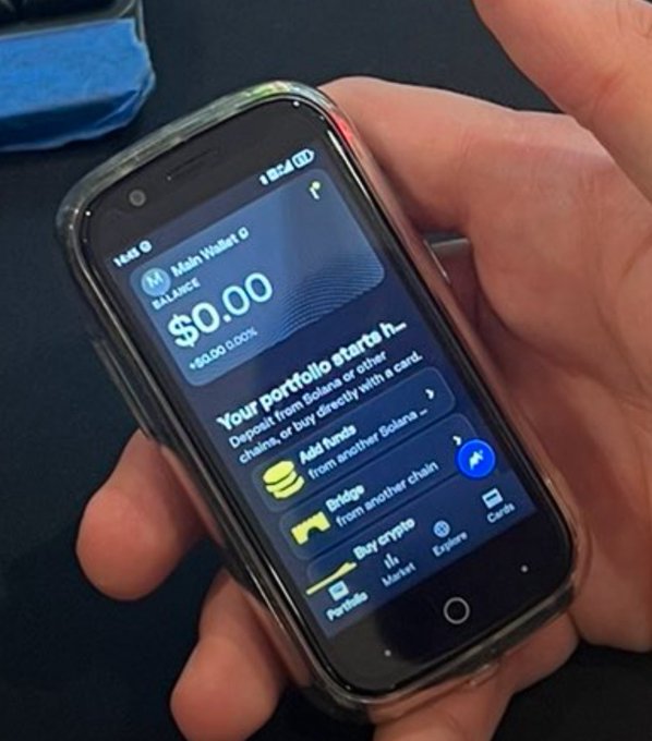 A hand holds a smartphone displaying a crypto wallet app with a balance of $0.00, showing options to add funds, bridge, or buy crypto on Solana.