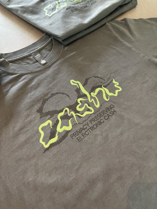 A close-up of a dark gray t-shirt featuring a yellow graffiti-style logo and the text "PRIVACY PRESERVING ELECTRONIC CASH."