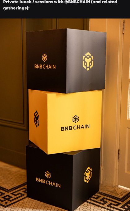 A stack of three black and yellow BNB Chain branded cubes sits indoors, representing the private lunch and sessions with @BNBCHAIN mentioned in the post about River Inc.'s LATAM networking week.