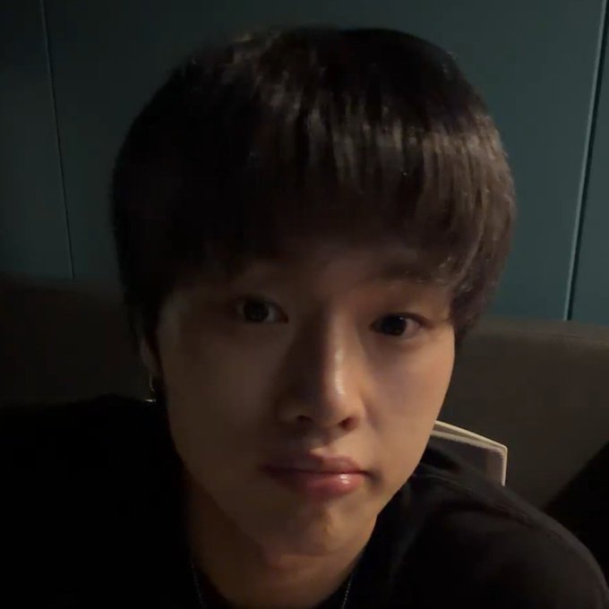 A close-up selfie of a young man with dark hair looking directly at the camera with a calm, slightly serious expression, wearing a black shirt and earring, with a dark cushioned background — seemingly reacting to a humorous "ripple" comment with a deadpan stare that adds to the comedic vibe of the post.