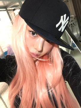 A young woman with long pastel pink hair takes a selfie while wearing a black New York Yankees baseball cap.