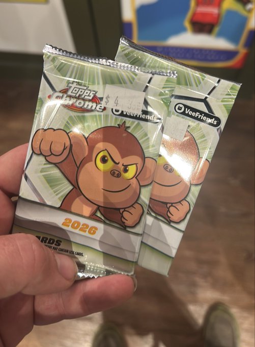 A hand holds two 2026 Topps Chrome "VeeFriends" trading card packs, each priced at $4, featuring cartoon monkey characters. This aligns with the post about opening @veefriends merchandise.