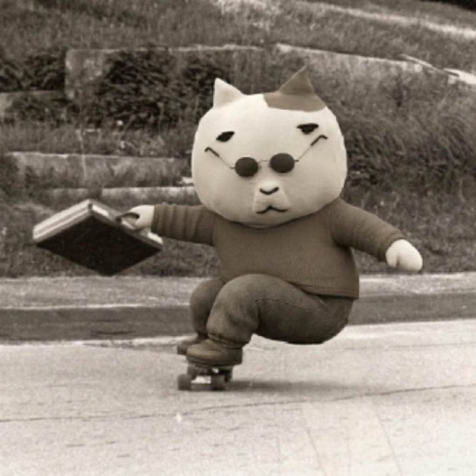 A whimsical photo of a plush cat toy wearing sunglasses, a brown sweater, and pants, posed riding a small skateboard while holding a black book, in a sepia-toned setting with stone steps.