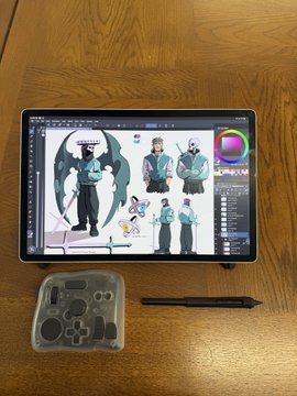 A digital artist working on a tablet displays character design sheets featuring a horned figure in three poses, alongside a stylus and controller case on a wooden desk. The image illustrates the creator's progress in building full character sheets for the "slimes" mentioned in the post, showcasing their design process.