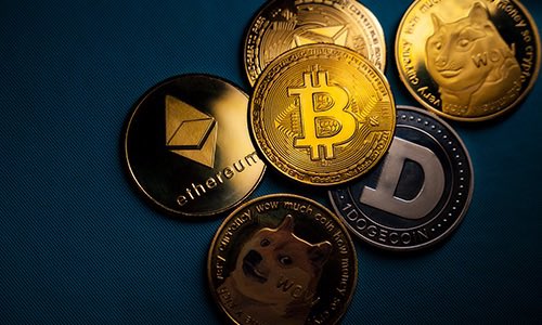 A collection of physical cryptocurrency coins including Bitcoin, Ethereum, and Dogecoin arranged on a blue surface.