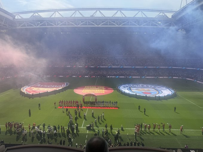 A football stadium with players lined up on the field, large banners for Arsenal and Manchester United, and 'THANK YOU UNITED FANS' displayed in the center.