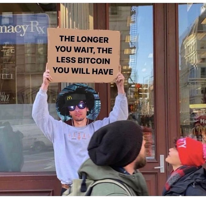 A street scene shows a person holding a cardboard sign reading 'THE LONGER YOU WAIT, THE LESS BITCOIN YOU WILL HAVE' above a McDonald's logo cutout with a face on it, while others stand nearby.