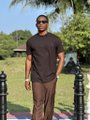 A low-resolution image of a man in a brown t-shirt and sunglasses standing outdoors near a row of black metal bollards.