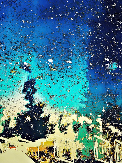 An abstract mixed-media painting featuring bright blue and turquoise tones with white, yellow, and green textured elements suggesting a landscape or sky scene.