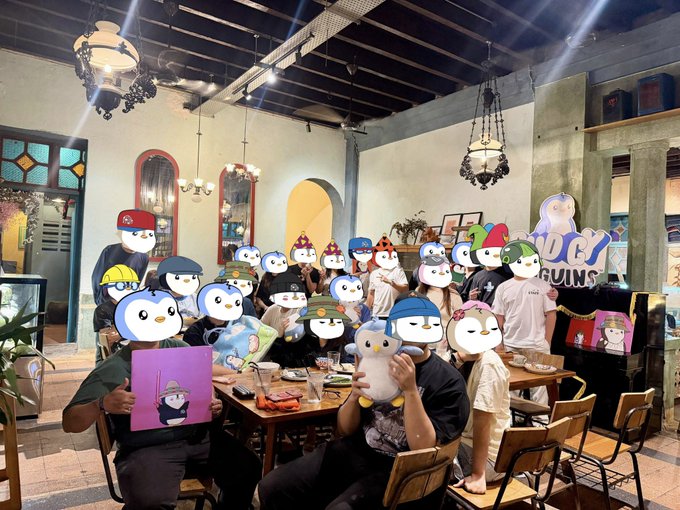 Group photo of attendees at a 'LUCY PENGUINS' event, with people wearing various penguin-themed masks and hats while seated at a restaurant table.