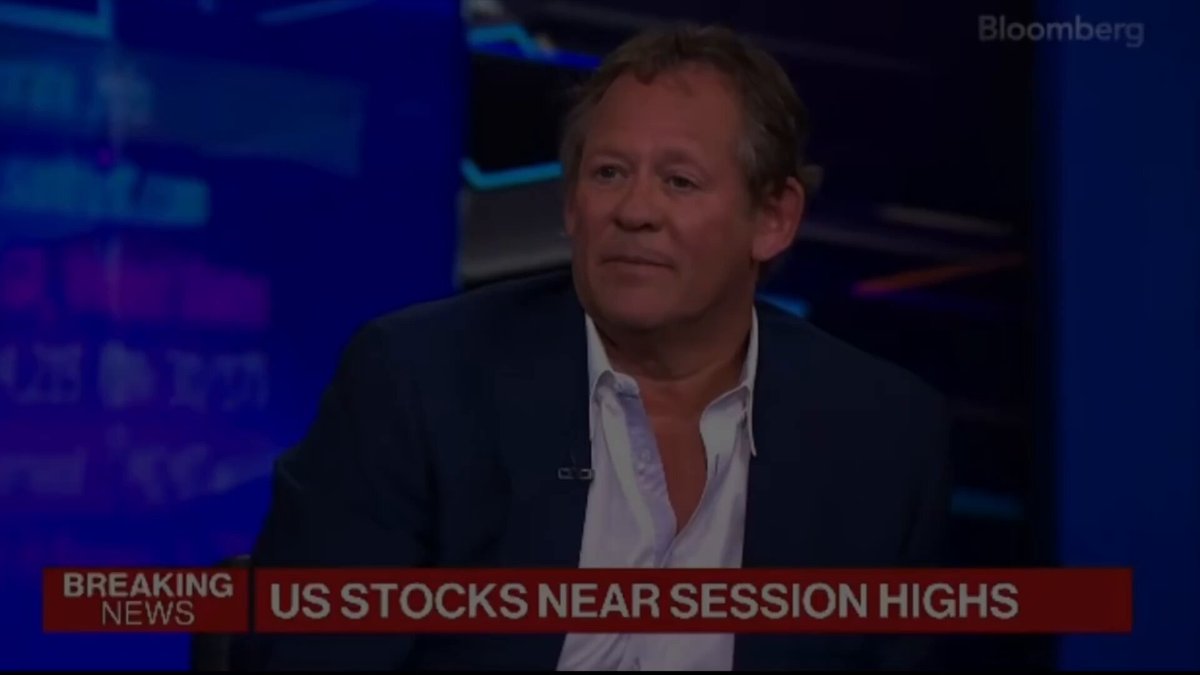 The image displays a man sitting down, possibly during an interview for a news program or television show. The focus of the conversation appears to be about the stock market, specifically involving Bitcoin as a cryptocurrency. There are several details visible in the image that can provide context regarding the topic being discussed, such as the news anchor's position and whether he is wearing a jacket. Additionally, there may be logos for other news outlets or sources, indicating a professional setting.