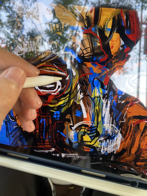A hand uses a stylus to create a vibrant, colorful abstract digital painting on a tablet screen, with reflections visible in the glass.