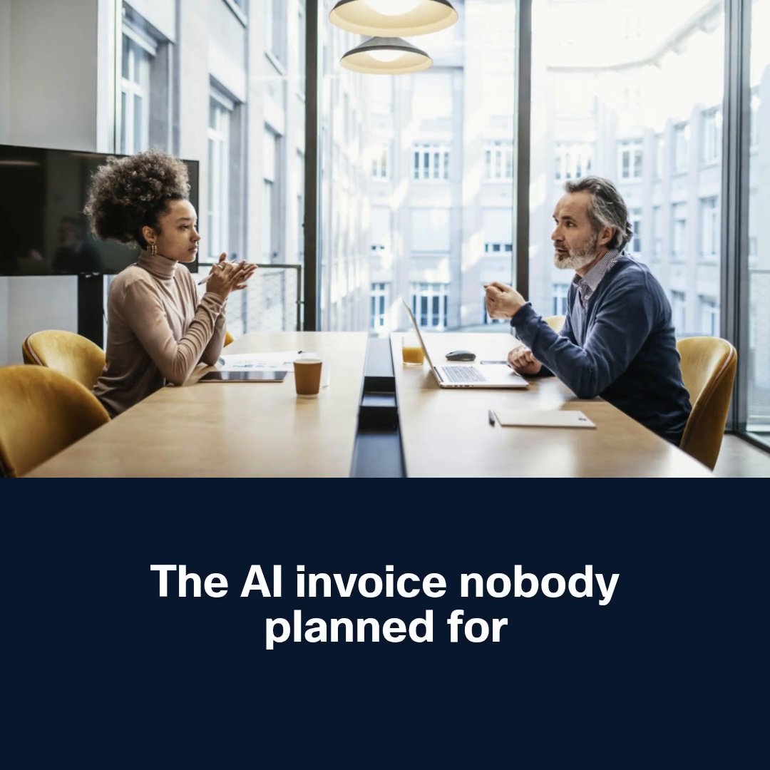 Two colleagues sit across from each other at a conference table in a sunlit office, engaged in conversation with documents, a laptop, and coffee cups in front of them. Below the scene, bold white text on a dark navy background reads "The AI invoice nobody planned for," reinforcing the post's message about the unexpected costs of AI infrastructure that organizations must strategically manage.