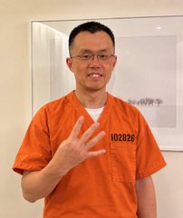 A smiling man wearing glasses and an orange prison uniform with the number "10282" displayed on it holds up his hand to show four fingers, likely celebrating the 10/10 date mentioned in the post. The image appears to be a mugshot-style photo referencing a Binance-related arrest.