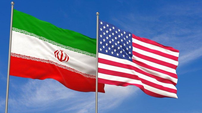 The flag of Iran flying alongside the flag of the United States against a blue sky.