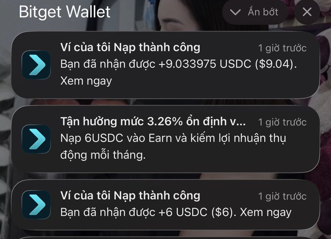 The image shows a Bitget Wallet notification popup in Vietnamese, displaying recent activity including successful deposits of "+9.033975 USDC ($9.04)" and "+6 USDC ($6)" received an hour ago, along with a promotional message about earning 3.26% interest by depositing 6 USDC into Earn. The notifications support the post's story about receiving an unexpected $15 in USDC deposits—totaling roughly $15.04—to a wallet that hadn't been used for a year, with the sender now humorously asking the unknown person to come forward so they can return the money.