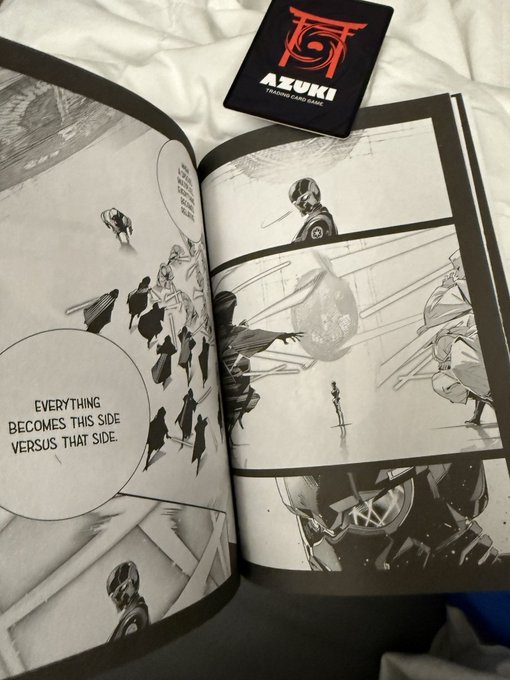 An open manga book showing black and white panels with the text 'EVERYTHING BECOMES THIS SIDE VERSUS THAT SIDE', accompanied by an 'AZUKI' Trading Card Game card.