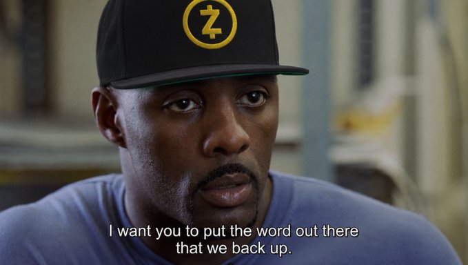 A still from a movie showing a man wearing a black and yellow "Z" cap and blue shirt, with subtitles reading "I want you to put the word out there that we back up."