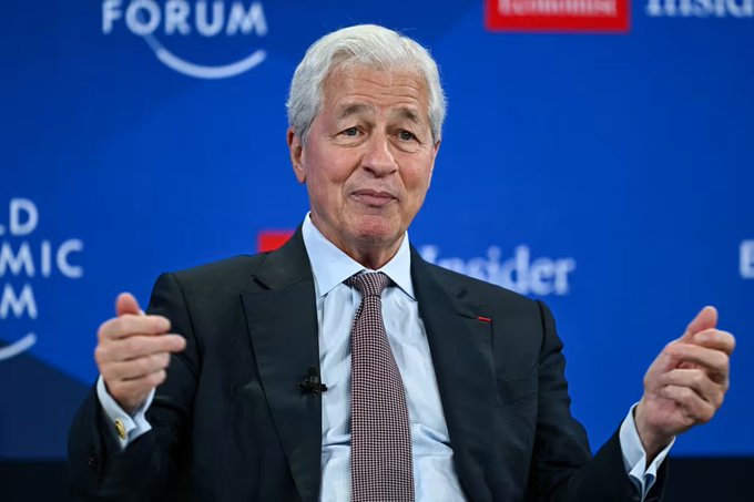 Jamie Dimon, CEO of JPMorgan Chase, speaks at the World Economic Forum, gesturing with both hands mid-discussion. The setting underscores the context of JPMorgan's hawkish Fed outlook, as Dimon's commentary carries significant weight in shaping market expectations for monetary policy.