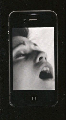 An artistic image showing a smartphone screen displaying a black-and-white close-up photo of a person's face with their mouth open.