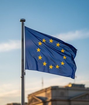 A European Union flag waves against a blue sky, symbolizing the regulatory authority behind the MiCA (Markets in Crypto-Assets) license that Binance failed to obtain, forcing it to cease serving customers in Poland, Italy, Spain, and France. The image visually represents the EU's regulatory crackdown on cryptocurrency exchanges operating within its member states.