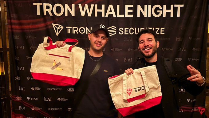 Two smiling men pose in front of a "TRON WHALE NIGHT" backdrop featuring TRON, Securitize, MetaMars, and S.AI logos, each holding a TRON-branded tote bag. The image likely celebrates a TRON DAO ecosystem event, complementing the post's announcement about the new automated circuit-breaker protocol designed to protect major smart contracts from flash-loan attacks and oracle price anomalies.