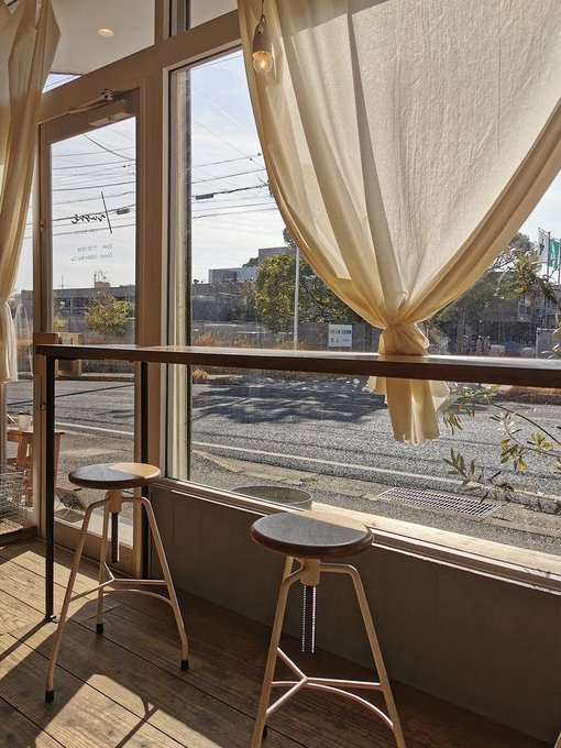 A cozy café or co-working space with two stools at a window bar, partially drawn cream curtains, and warm sunlight streaming in. The handwritten reversed text on the glass reads "OPEN" and "SUNDAY 8:00 am - 4:00 pm," suggesting a quiet, reflective spot perfect for the post's message about taking a mindful break, building connections, and giving yourself grace during a tough week in crypto.