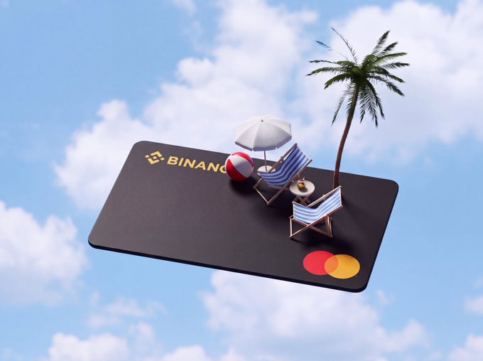 A 3D illustration of a black Binance card functioning as a miniature beach platform, complete with two striped lounge chairs, an umbrella, a beach ball, and a palm tree, floating against a cloudy sky.