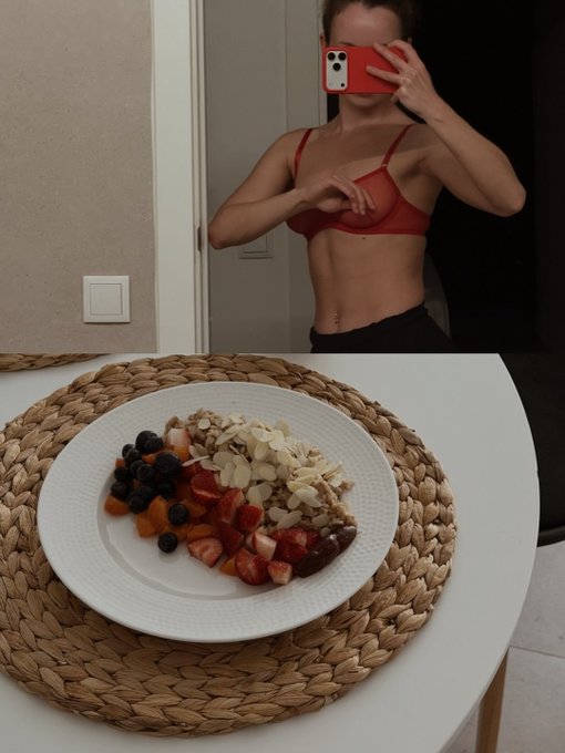 A mirror selfie of a person with a red phone case, showing a plate of food with strawberries, blueberries, and almonds on a woven placemat.