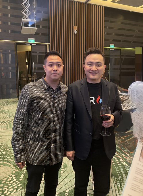 Two men pose together at an indoor event, with the man on the right wearing a black blazer over a t-shirt featuring the "TRON" logo and holding a glass of red wine. The caption "GM FINALLY MET @justinsuntron IN PERSON!" along with the mention of an HTX VIP dinner, suggests this is a photo from that event featuring Tron founder Justin Sun on the right.