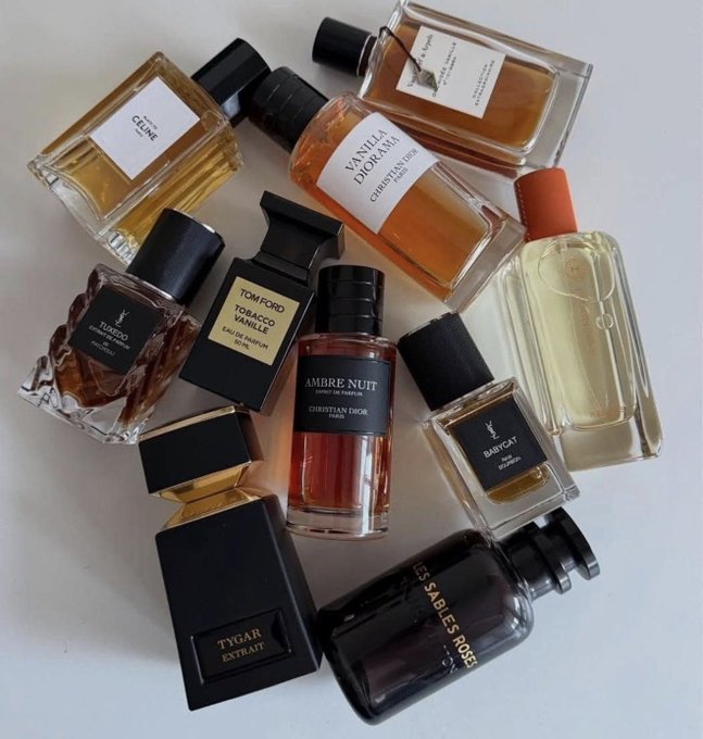 A flat lay arrangement of various high-end perfume bottles, including brands like Christian Dior 'Ambre Nuit' and 'Vanille Diorama', Tom Ford 'Tobacco Vanille', YSL 'Babycat' and 'Tuxedo', and Hermes 'H24'.