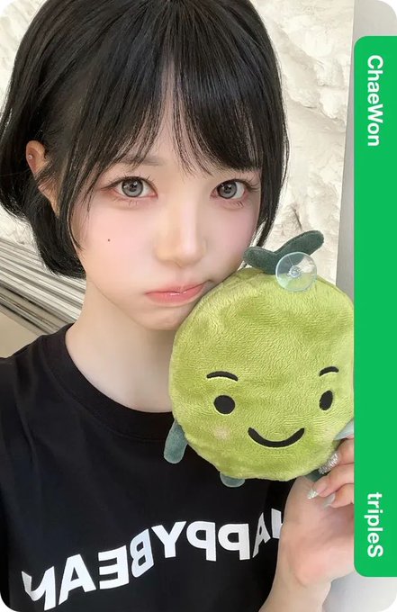 A young woman with short dark hair and a black t-shirt holds a plush toy resembling a green fruit character with a smiley face; text overlays read "ChaeWon" and "tripies".