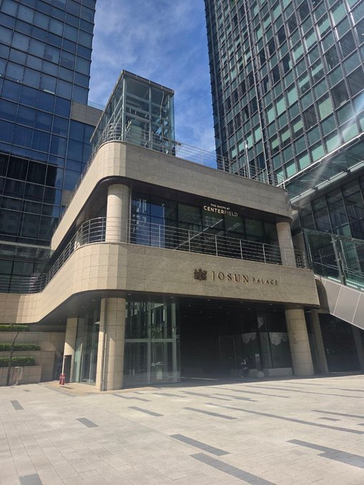 The exterior entrance of a building displays signs for 'SANWA CENTERFIELD' and 'JOSUN PALACE' in both English and Korean, surrounded by modern glass skyscrapers.