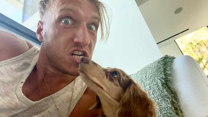 A man makes an exaggerated wide-eyed expression while his small brown dog playfully licks his teeth, with no visible text or numbers in the image relating to the Bitcoin "$100 Million Trade" post.