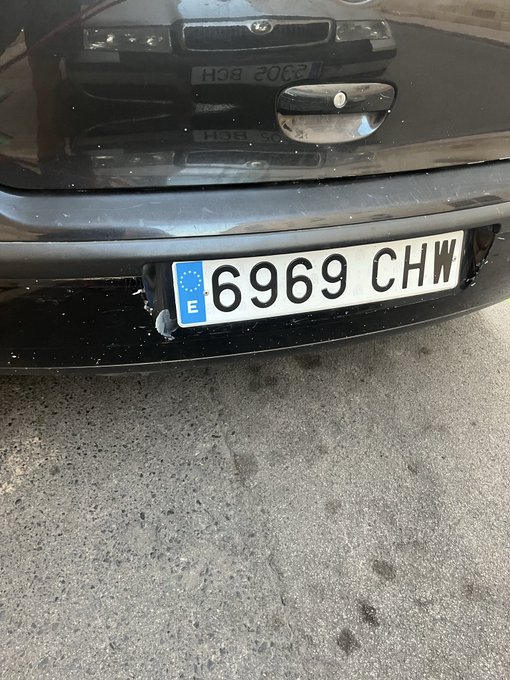 A close-up of a Spanish license plate reading '6969 CHW' on the back of a dark gray car, with a 'V' sticker on the bumper.