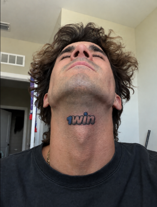 A young man tilts his head back to reveal a tattoo on his neck reading "1win," a reference to an outdated logo, playfully supporting the post's claim that the brand "changed the logo a long time ago."