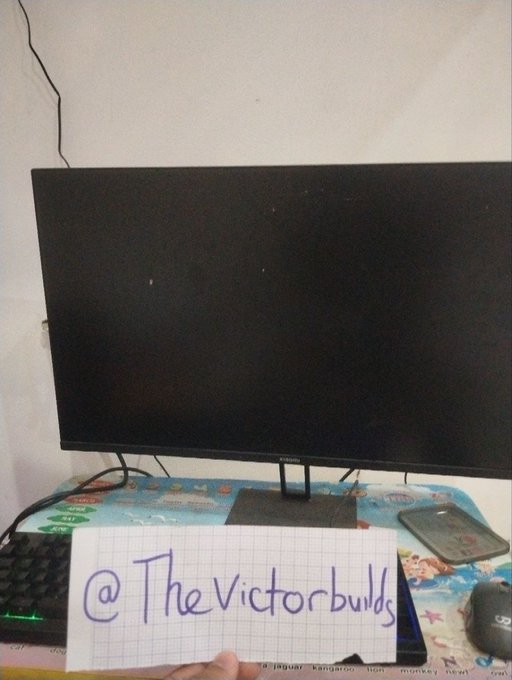 The image shows a computer monitor displaying a black screen, with a handwritten note in front of it reading "@TheVictorbulbs" on grid paper, alongside a keyboard and smartphone on a desk with a blue patterned cloth. The caption appears unrelated to the accompanying post about Circle's stablecoin business and USDC profitability, showing instead a casual setup photo likely meant for social media branding.
