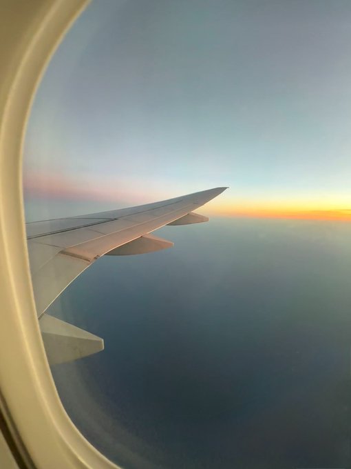 A view from an airplane window showing the wing against a gradient sunset sky with orange and blue hues.