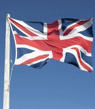 The image shows a waving United Kingdom (Union Jack) flag against a clear blue sky, symbolizing the British context of the news about U.K.-based Bitcoin treasury company Satsuma delisting from the London Stock Exchange. The flag's prominent display visually represents the company's U.K. origins as it prepares to exit the LSE following a High Court-approved $41 million payout.