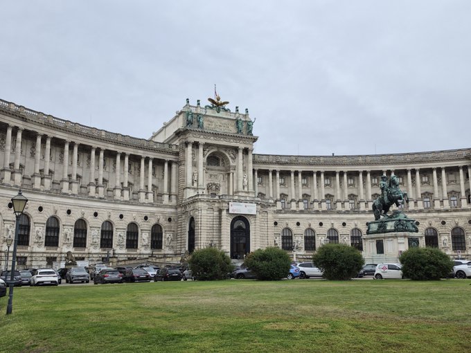The Hofburg Palace in Vienna, a large curved Baroque-style building with columns, featuring a statue of Prince Eugene on horseback in front.