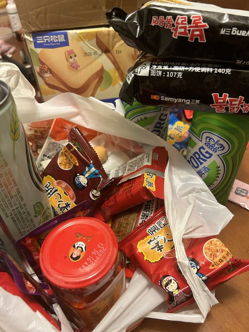 A haul of Chinese snacks and instant noodles including Samyang (三养) ramen, Three Squirrels (三只松鼠) products, and Master Kong (康师傅) packages spilling out of a shopping bag. The post reflects on how spending only 10 USDT on this entire bag of food feels surprisingly cheap after being used to cryptocurrency-denominated transactions, making the user feel disconnected from real money.