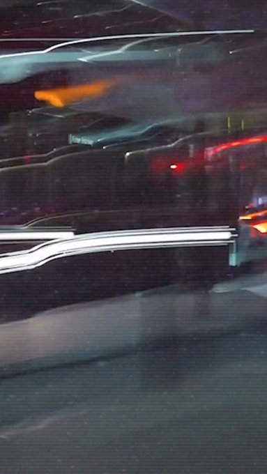 A blurry nighttime photograph taken from inside a moving vehicle, showing streaks of red and white lights from other cars and street lighting.