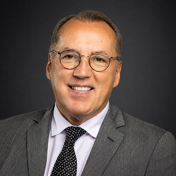 The image features a man wearing glasses and a suit jacket with a tie. He has a smile on his face as he looks directly at the camera. The caption below the photo reads, "LATEST:Hive Chairman Frank Holmes says Bitcoin represents financial sovereignty and individual freedom, offering an alternative to centralized control by governments and traditional financial institutions." This statement is related to the image because it suggests that Bitcoin could be seen as a symbol of financial independence and personal choice in a world where centralized authority often dominates.