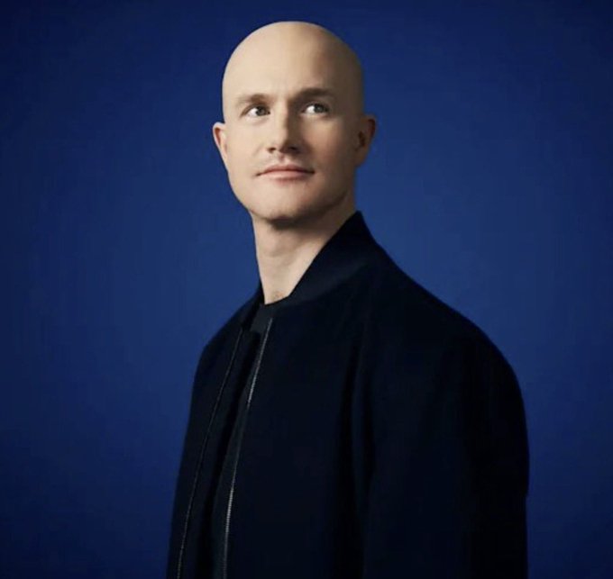 A bald man in a dark jacket looks upward against a blue background.