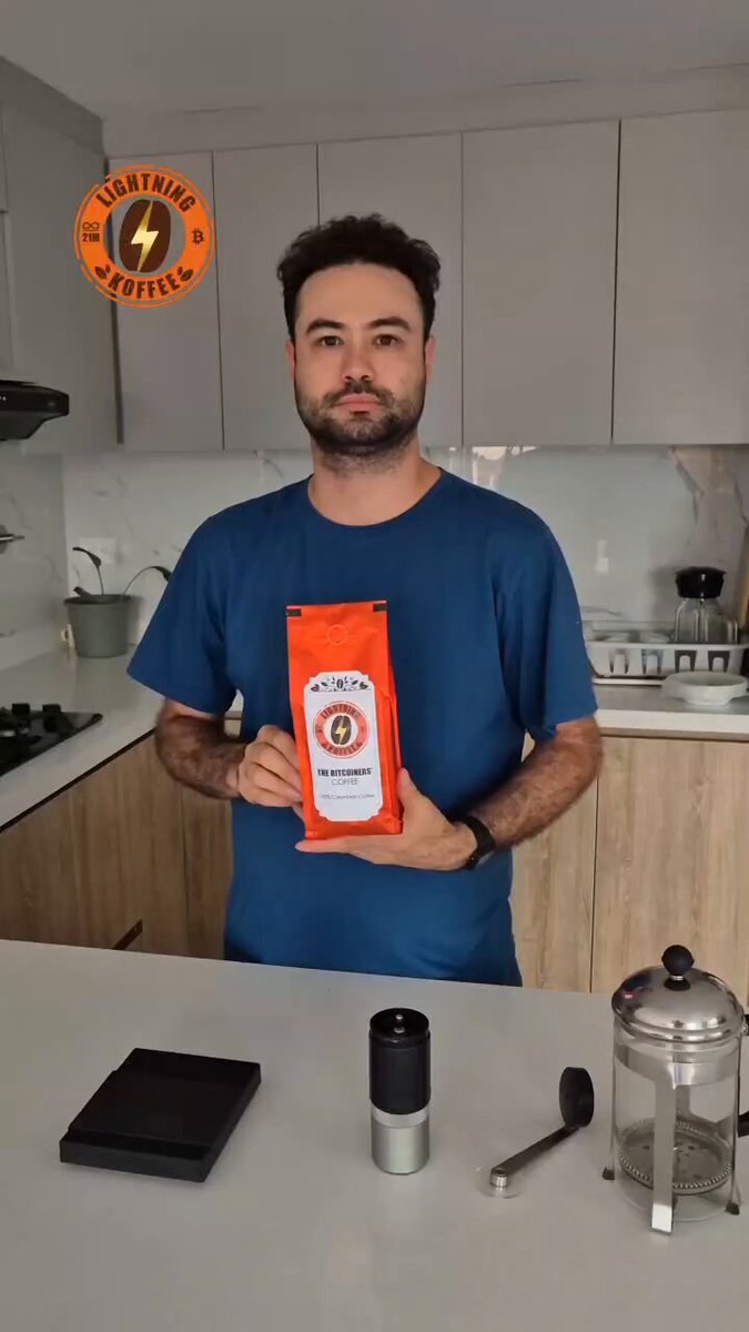 The image features a man standing at a kitchen counter, holding up an orange bag of coffee beans. The background includes white cabinets and various kitchen appliances such as a microwave and a blender. There are also two cups placed nearby, one on the countertop and another in front of the man. The post appears to be promoting Bitcoin's circular economy by encouraging people to make their own coffee at home using a French press instead of purchasing pre-packaged coffee from stores or cafes.

The image is accompanied by an orange logo that reads "LightningKoffee", suggesting that the coffee beans are made with lightning bolt energy, which is a Bitcoin mining company. The post also mentions shipping being free within the USA and encourages people to support Bitcoin's circular economy by making their own coffee at home using a French press instead of purchasing pre-packaged coffee from stores or cafes.