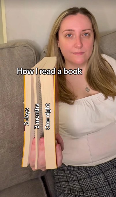 A woman sits on a couch holding open a book that humorously displays the "How I read a book" timeline across its pages, marked with text reading "2 days," "3 months," and "One night" to illustrate how her reading pace varies.