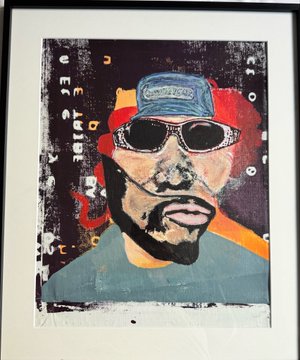 A framed mixed-media portrait painting depicts a bearded man wearing a blue "Good Year" cap and dark sunglasses, set against a dark background with red and orange accents and scattered white text fragments. The artwork aligns with the artist's "Painting the Noosphere" daily creative practice, representing a personal piece now being documented as part of the project's evolution toward exhibition.