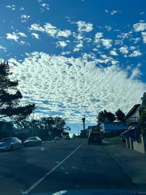 A view from inside a car driving down a road, featuring a stunning sky filled with textured, rippled clouds over a suburban street.
