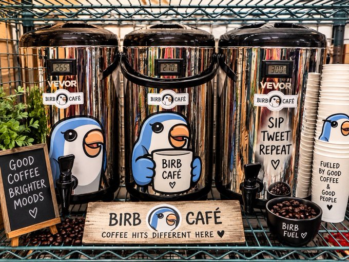 A coffee station setup features "BIRB CAFE" branded stainless steel urns with "Sip Tweet Repeat" and "BIRB CAFE" text, along with matching paper cups and signs reading "GOOD COFFEE BRIGHTER MOODS" and "FUELED BY GOOD COFFEE & GOOD PEOPLE."