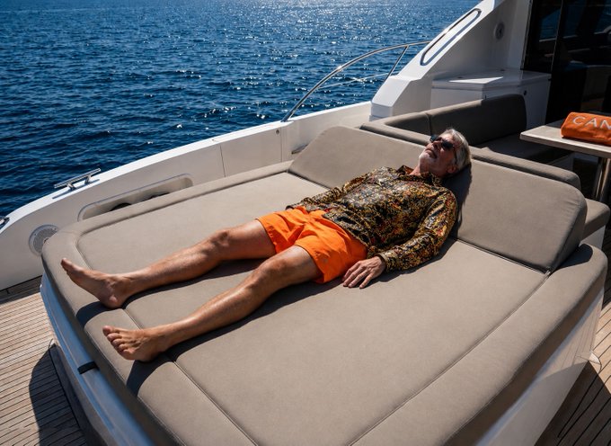 The image shows a man lying down on a boat, wearing an orange shirt and shorts. The boat appears to be a yacht or a large motorboat with a white cabin. In the background, there are some other boats visible. The photo also contains text that reads "BREAKING: @saylor is headed to Cannes for the summer after selling 32 Bitcoin." This suggests that the man might have recently sold Bitcoins and is now preparing for his trip to the picturesque island of Cannes.

The image seems to be a combination of elements from different sources, such as a photo of the man on the boat and text about him selling Bitcoins. The overall scene conveys a sense of relaxation and leisure, with the man enjoying his time on the boat while contemplating his recent Bitcoin transaction.